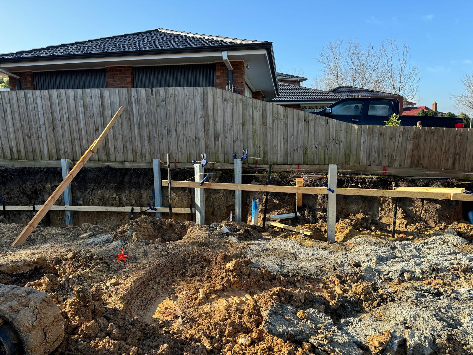 Steel retaining wall posts braced and set in a trench along a timber boundary fence