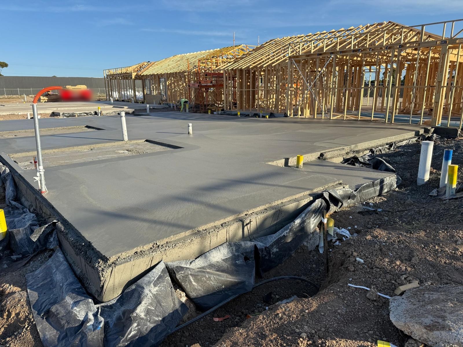 A freshly poured and finished house slab with timber house frames going up behind it